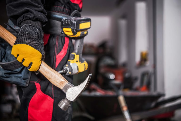 Closeup of Construction Worker Holding a Hammer in His Right Hand. Electric Screwdriver Hanging on a Tool Belt in the Background. Professional Building Tools Theme.