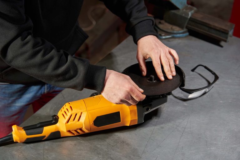 The hands of a caucasian worker install a cutting disc on an angle grinder on a locksmith workbench. goggles lie. High quality photo